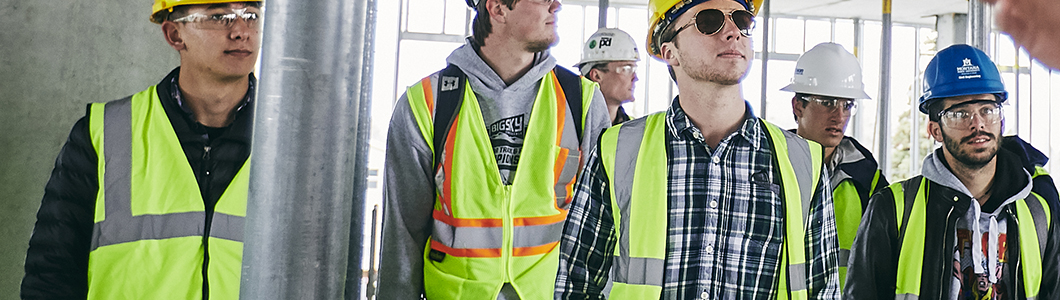 A group of students in hard hats and safety gear inspect a dorm construction site on MSU's campus.