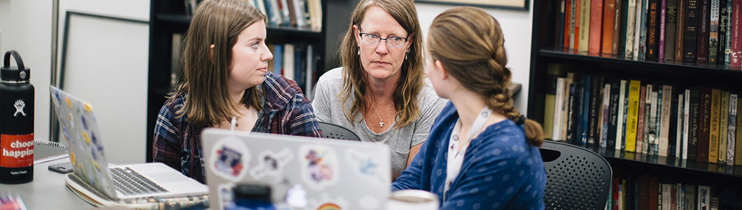 A professor and two students discuss a question in the library archives.