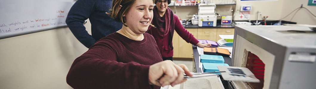 A student places an experiment sample into a machine using tongs.