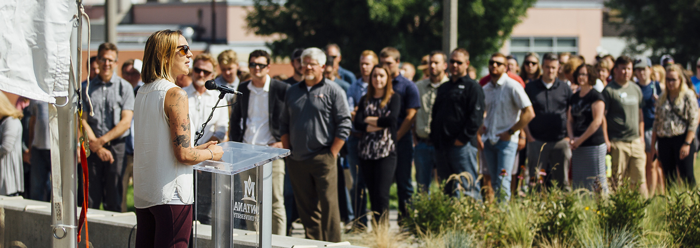 A woman stands at a podium outside, talking to a crowd of people.