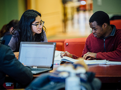 Students work around a laptop in a building lobby.