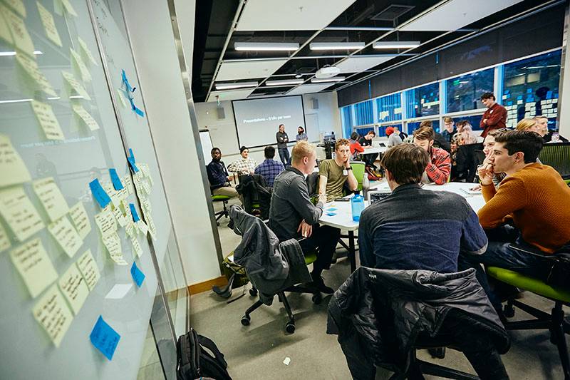 interactive workshop for students in Jabs Hall 207. Students are sitting in groups and there are sticky notes on the windows and walls.