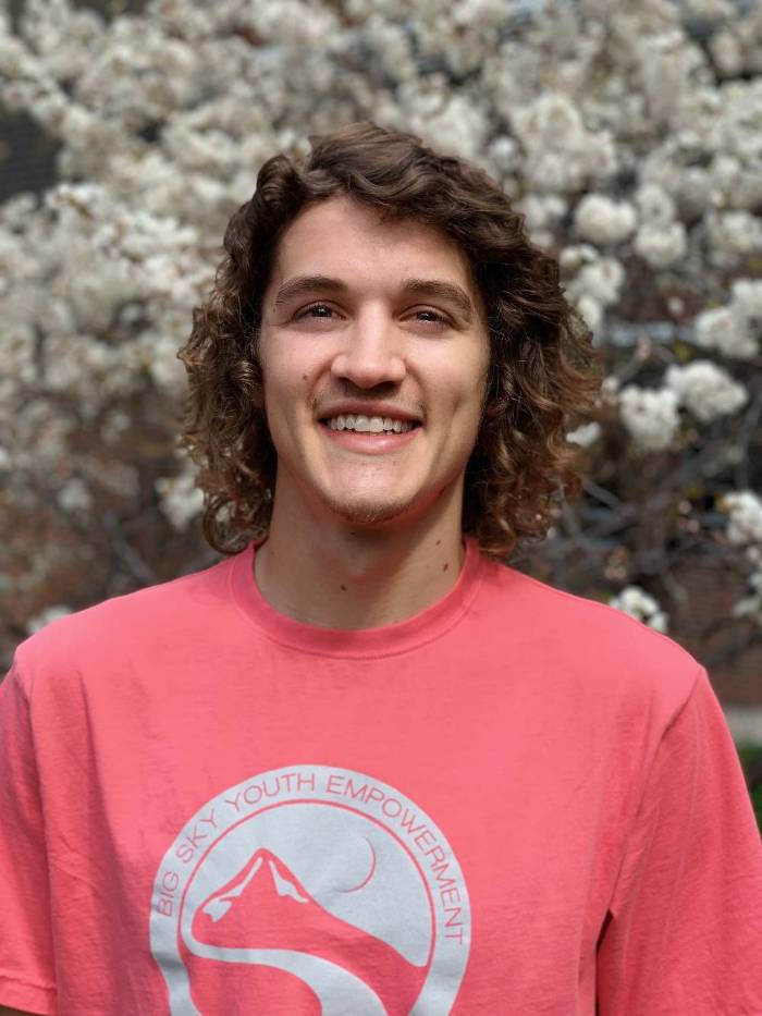 Smiling man with brown hair wearing a pink Big Sky Youth Empowerment t-shirt