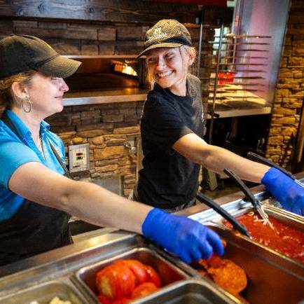 two female culinary services workers making pizzas