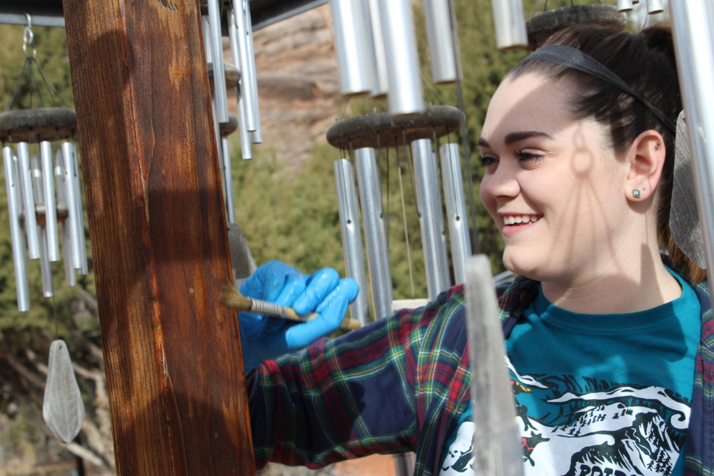 Student Staining some wood while smiling.