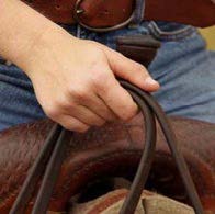 Person on a horse holding reins togther with one hand firmly grasping and their thumb on top