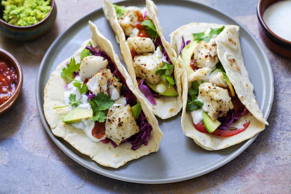 A plate with three soft shell tacos containing meat and vegetables.