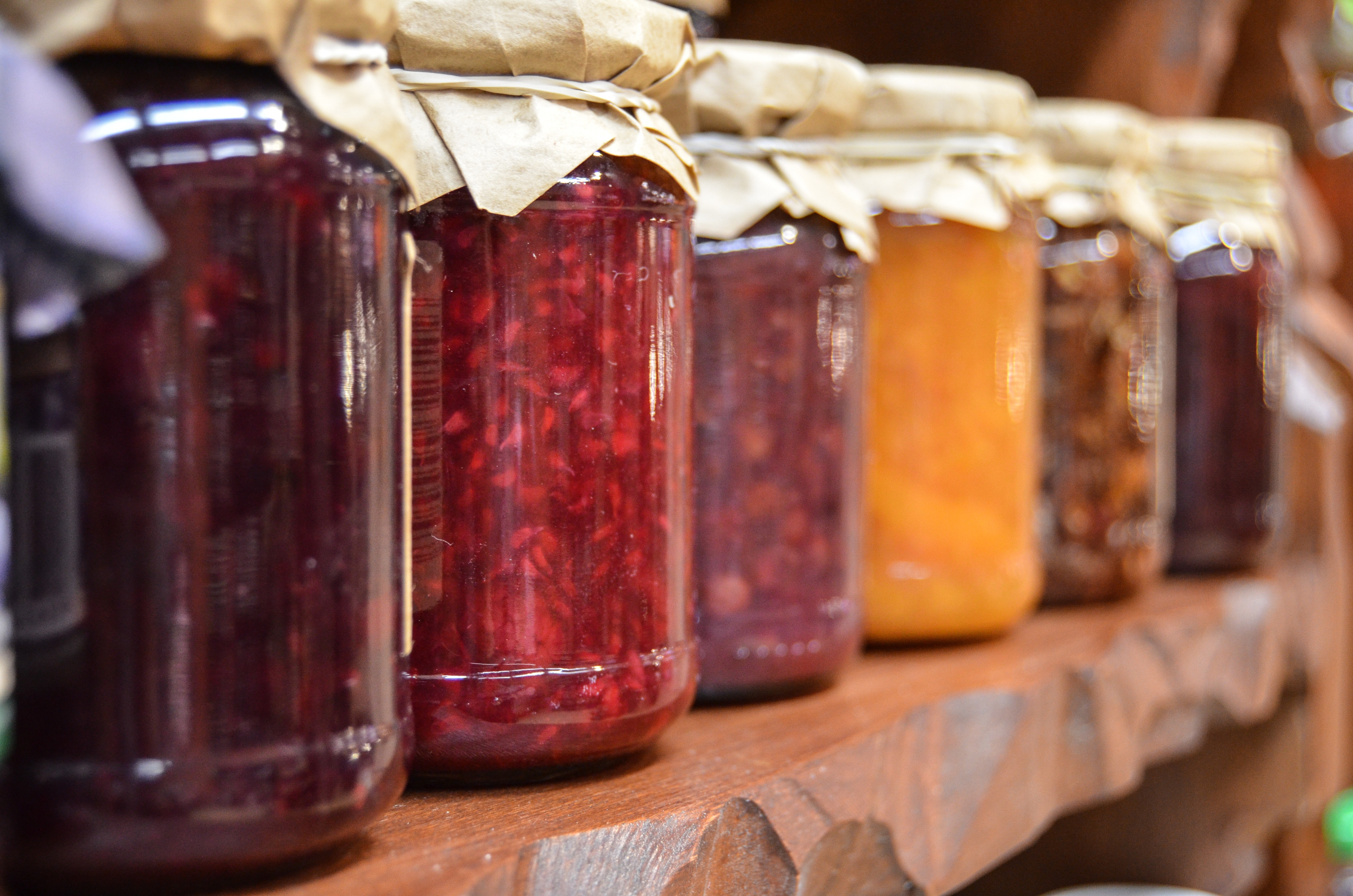 canned food in glass jars with cloth lids sitting on a wooden shelf