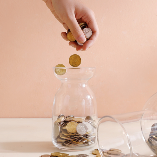 Photo of a person dropping coins into a coin jar. 