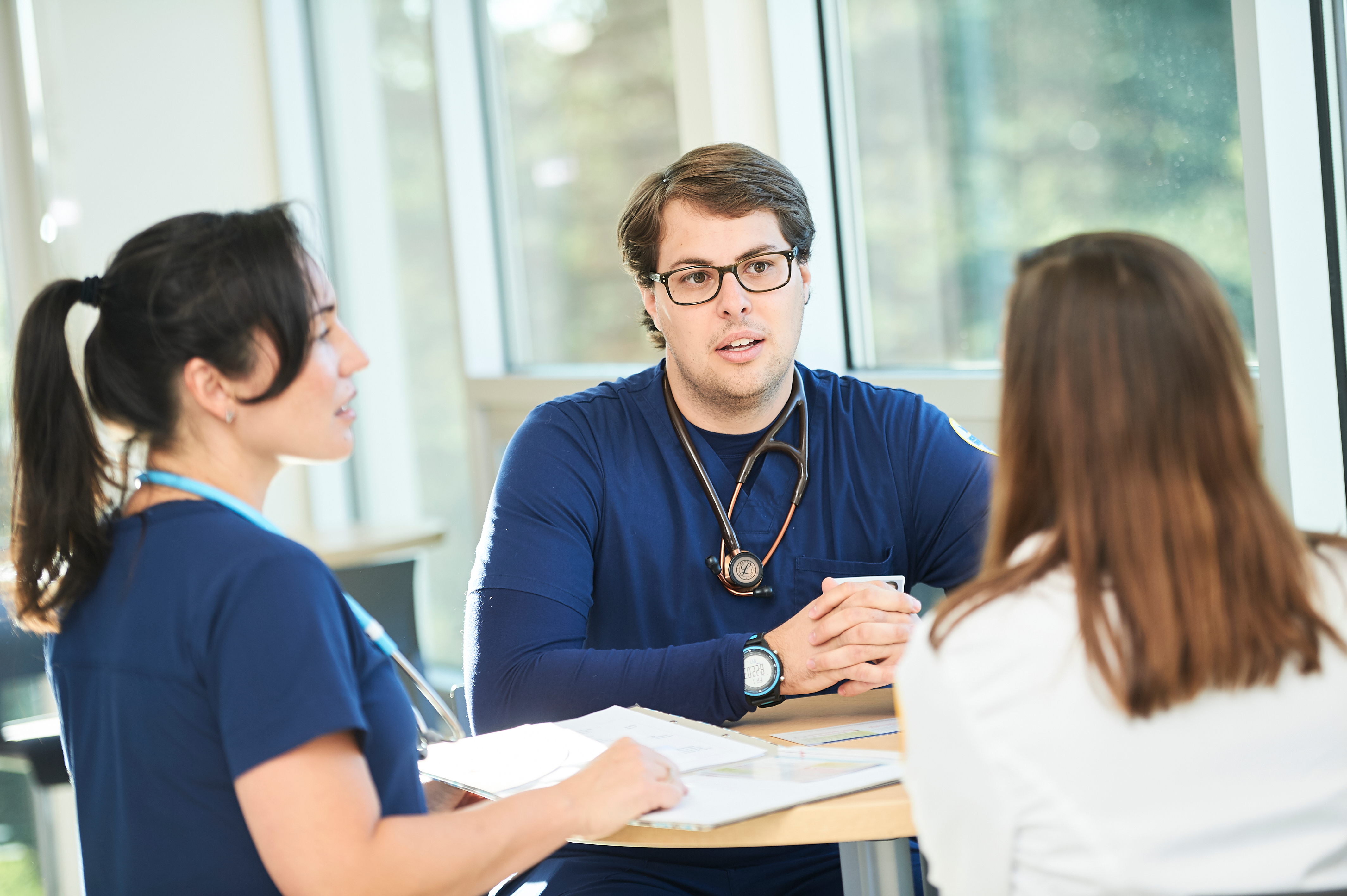 Three nursing students in scrubs talking around a table