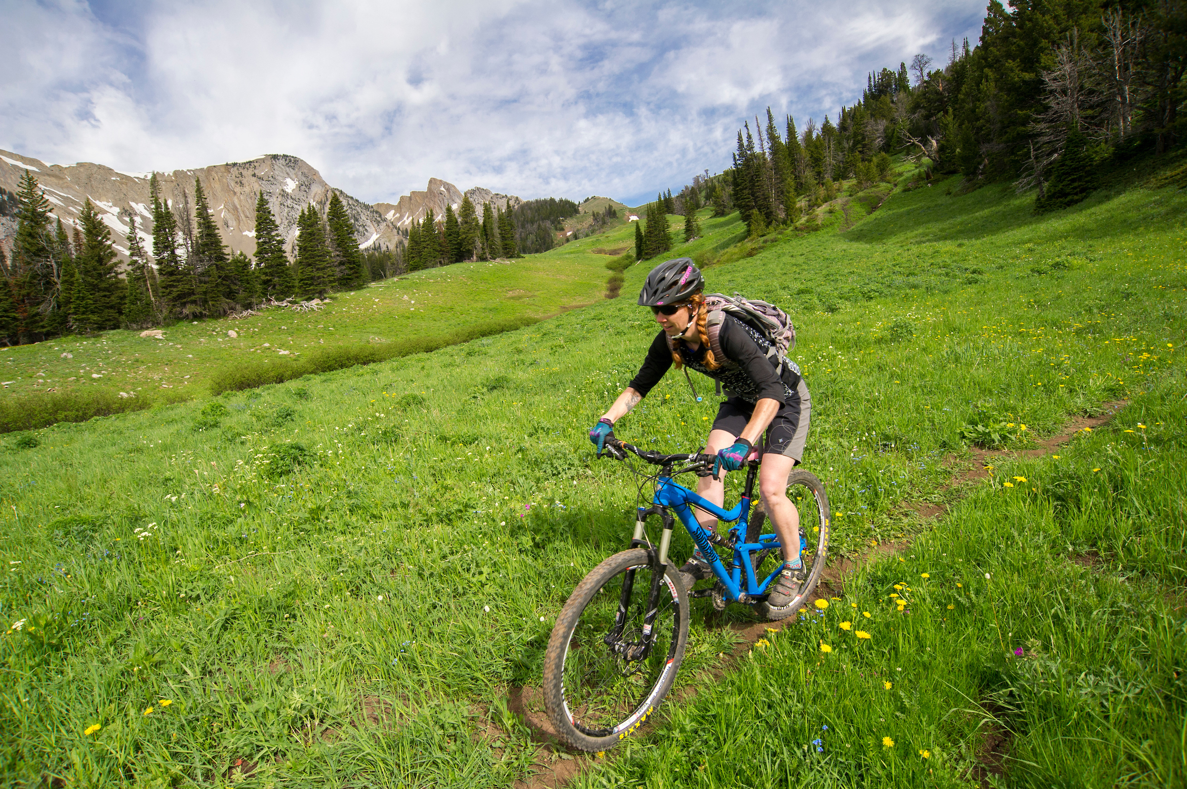 woman mountain biking through grass with mountains