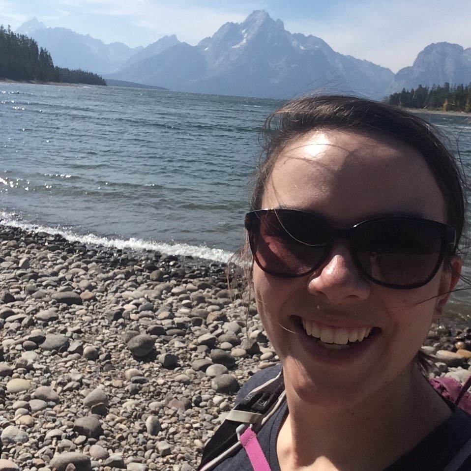 Meredith smiling at the camera with sunglasses on. The tetons are in the background.